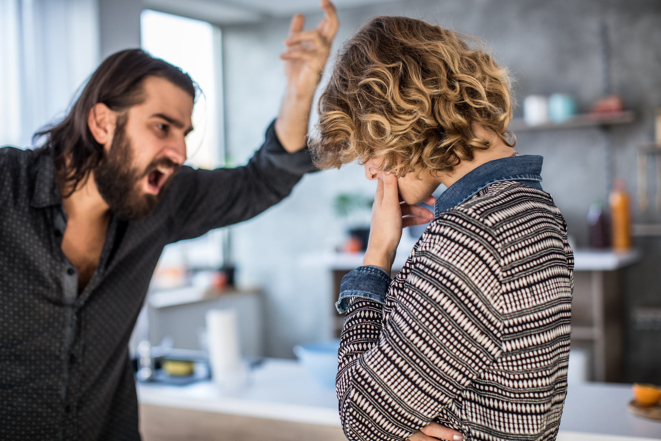 A person with long hair angrily gestures at another person with curly hair who looks upset, illustrating relationship conflict in a home setting