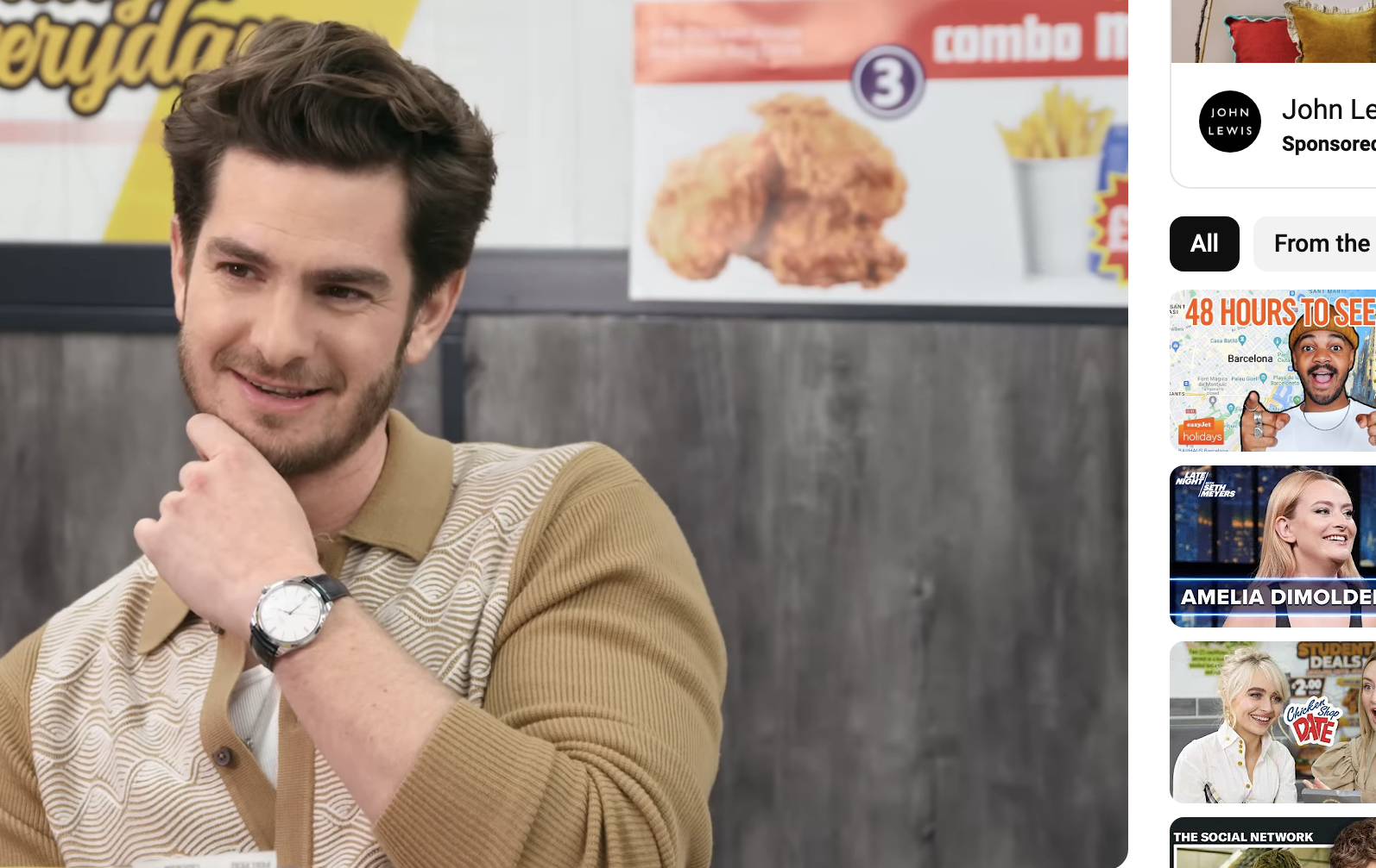 Andrew Garfield smiling in an interview for &quot;Chicken Shop Date&quot; with Amelia Dimoldenberg, seated at a table with food