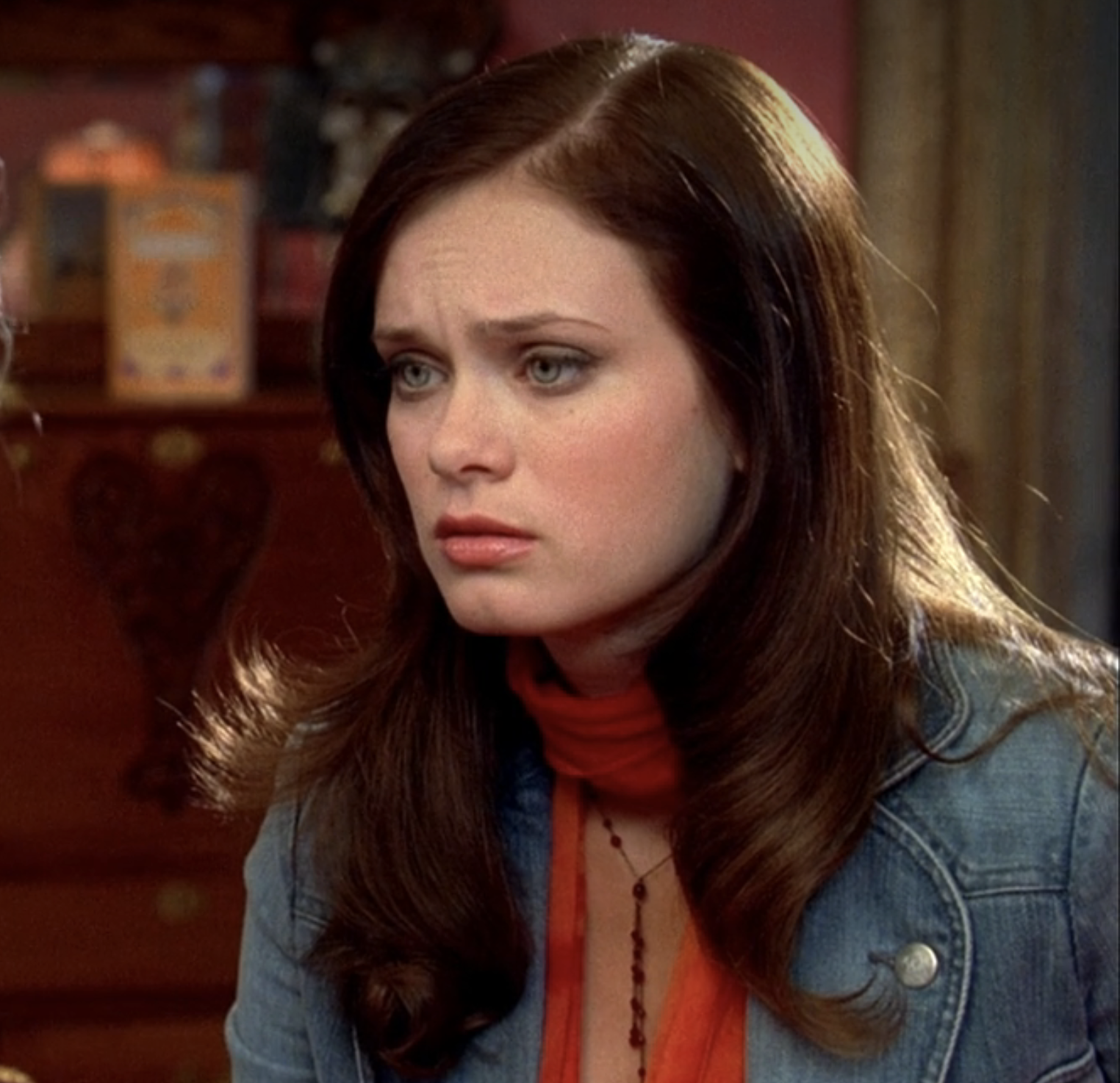 Sara with long hair and a worried expression wears a denim jacket and a scarf