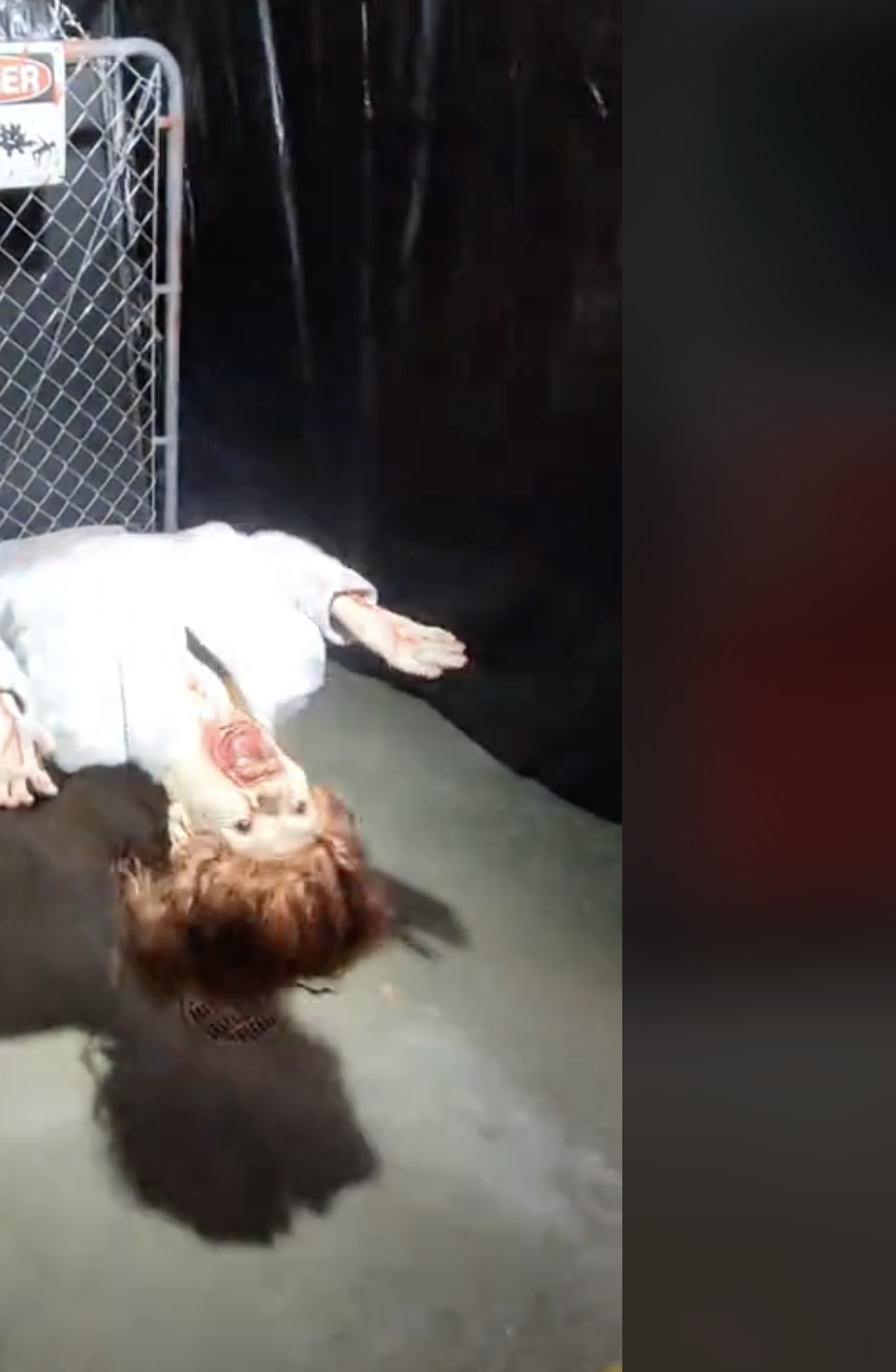 Haunted house prop featuring a lifelike, scary figure hanging upside down from a fence, adding an eerie ambiance