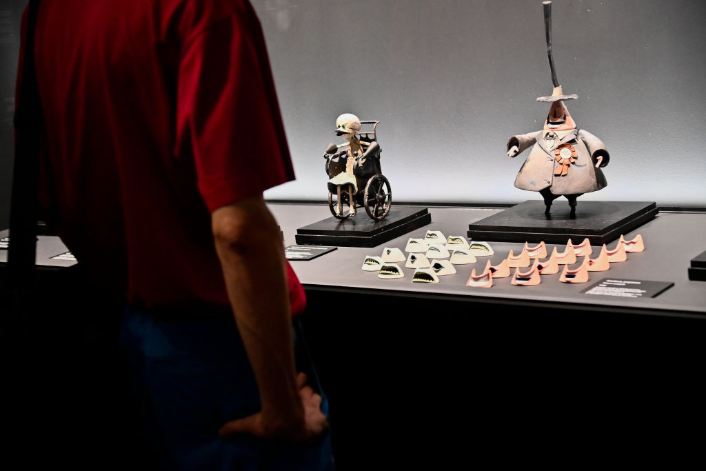 A person observes Tim Burton-style figurines with various mini spectacles displayed in a museum exhibit