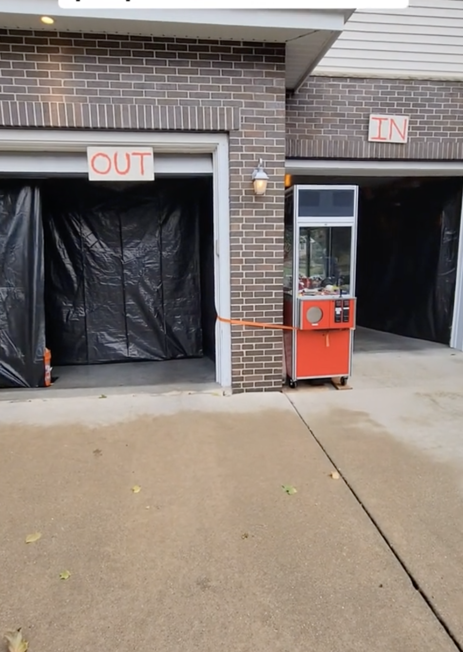 Garage with open doors marked &quot;In&quot; and &quot;Out,&quot; decorated for Halloween. A red arcade machine is visible. Text reads &quot;Homemade props haunted house&quot;