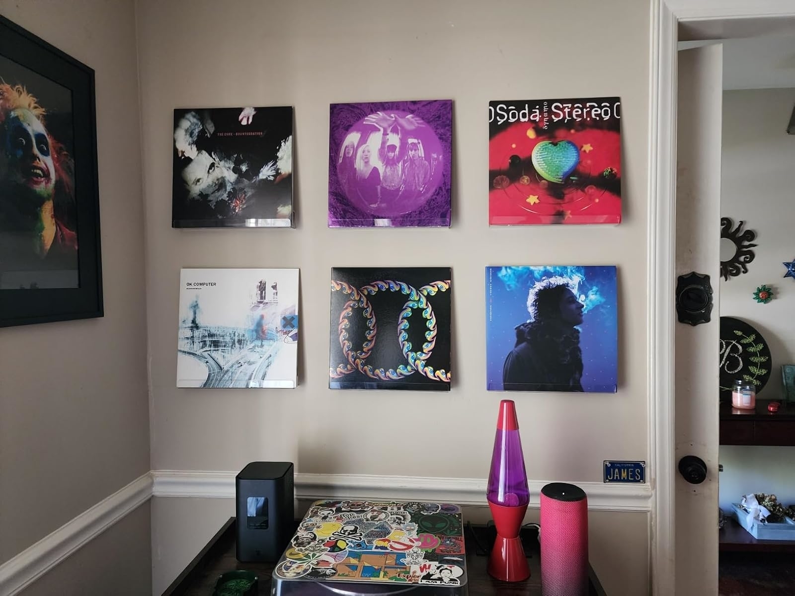 Wall with framed album covers and decorative items on a shelf, including a lava lamp and a black speaker