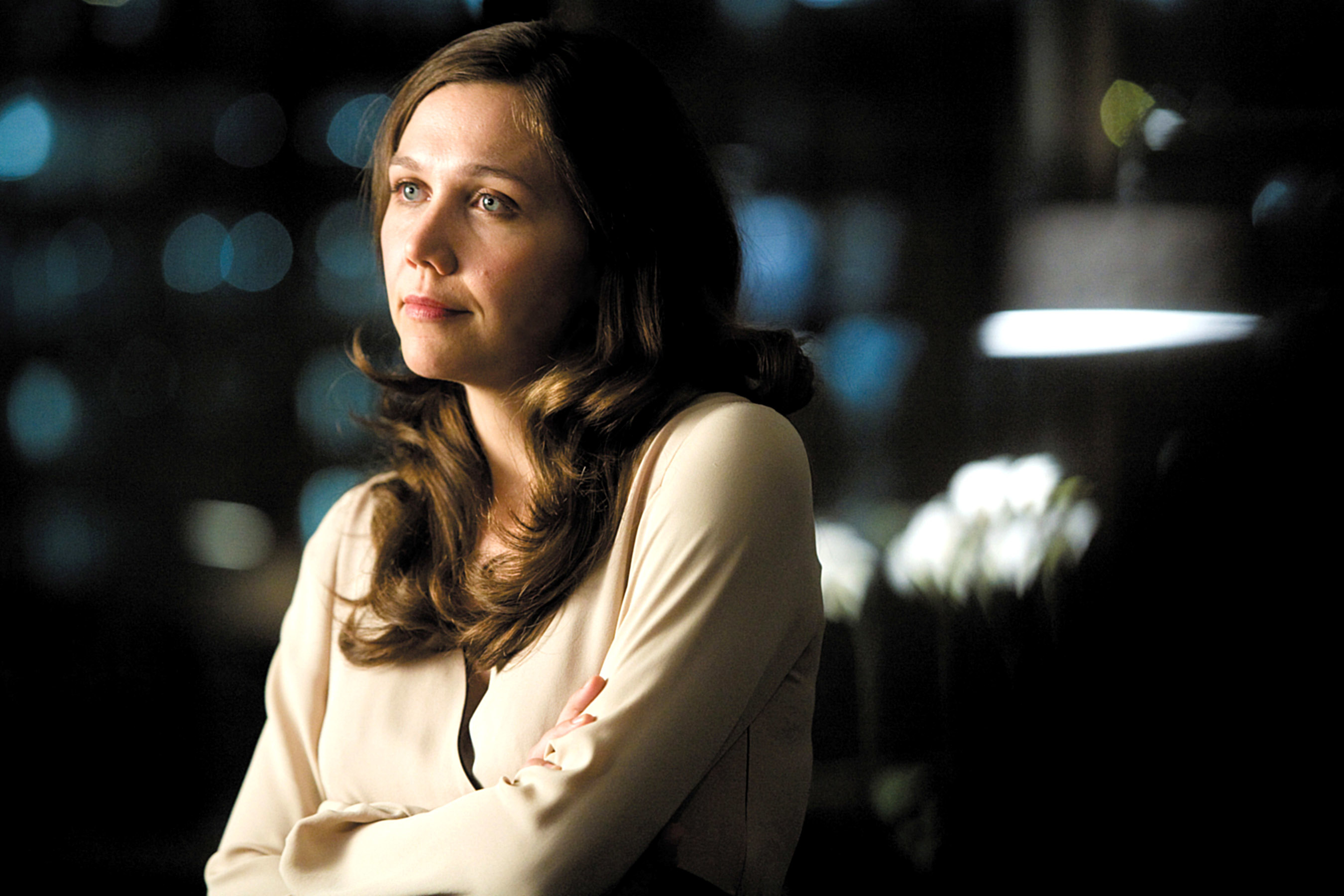 Maggie with long, wavy hair wearing a long-sleeved blouse, arms crossed