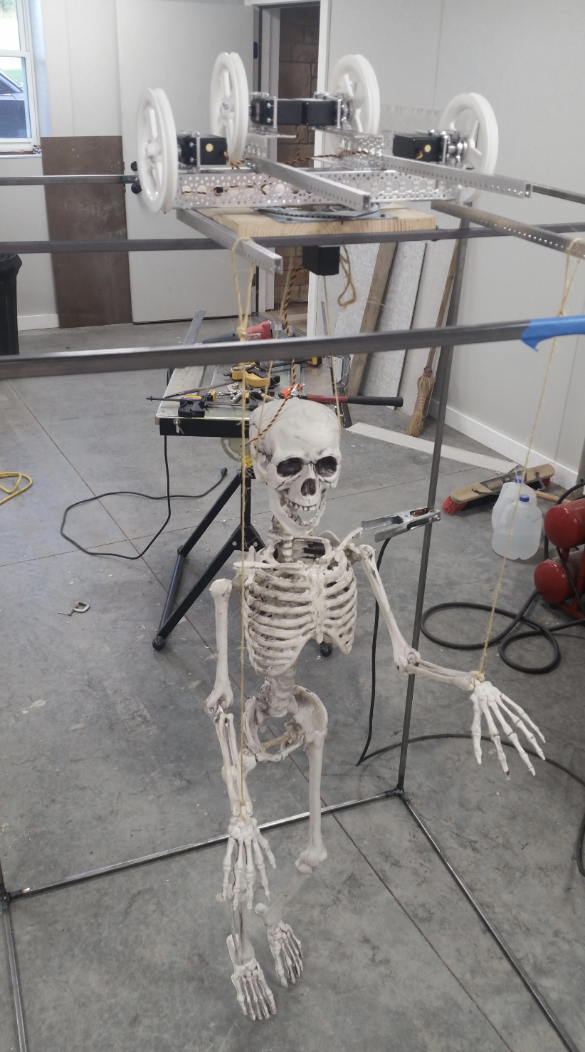 Skeleton hanging from a frame, suspended with string, next to a workbench and tools in a workshop setting