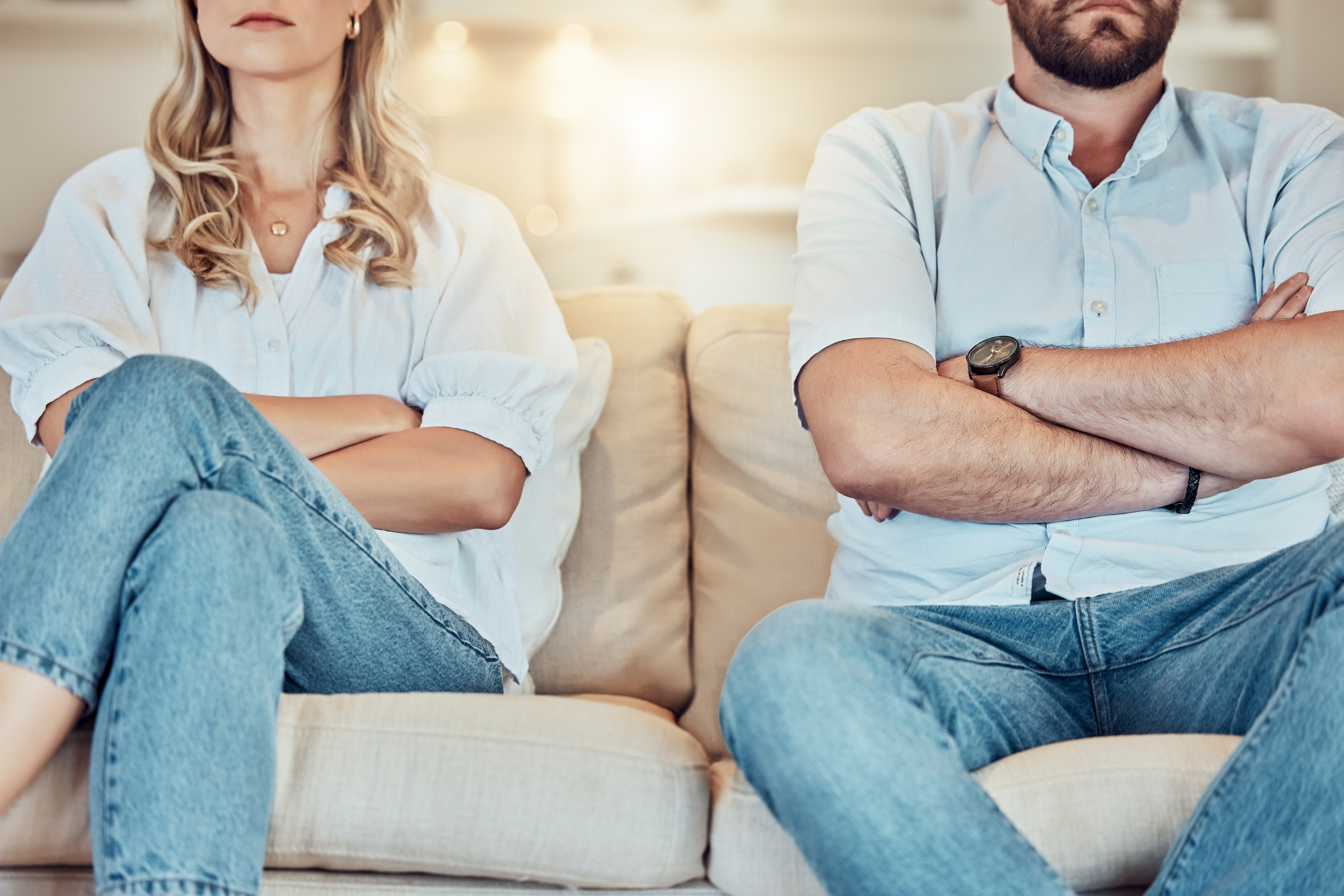 A couple sitting apart on a couch with crossed arms, showing signs of tension