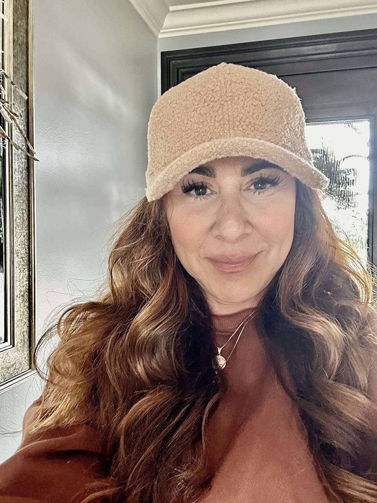 A person wearing a fuzzy cap and a brown top smiles while indoors