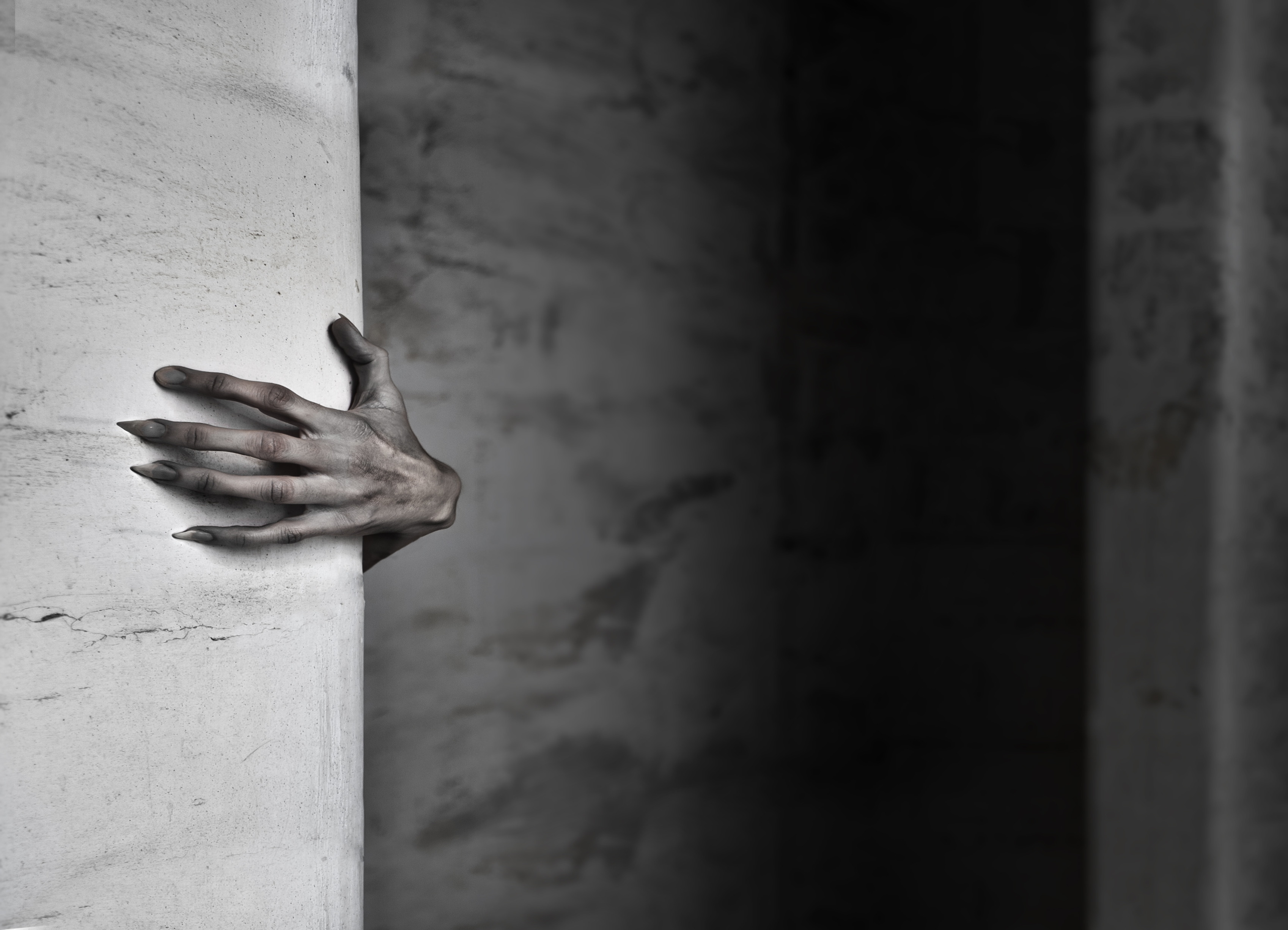 A realistic, eerie hand with claw-like fingers emerging from behind a stone pillar in a dimly lit setting