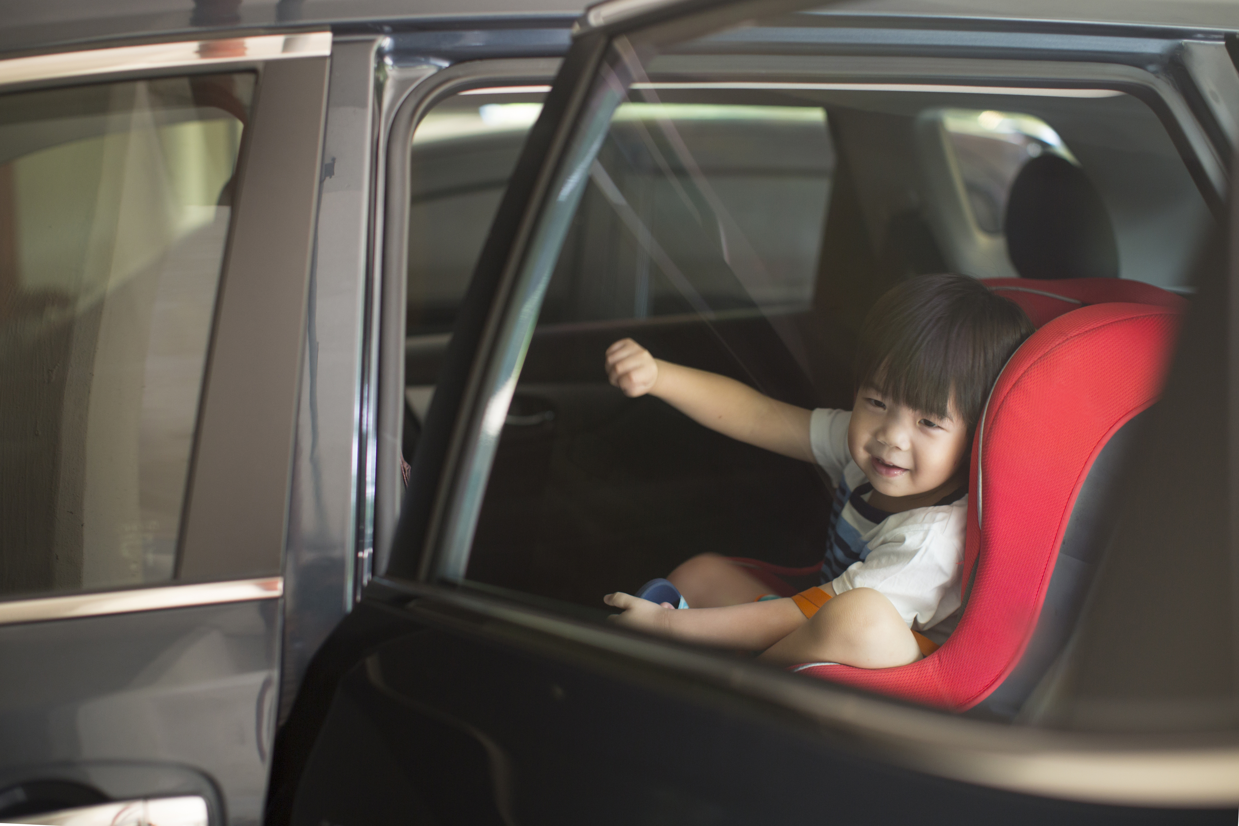 Child sitting in a car seat, smiling and raising a fist in joy inside a car