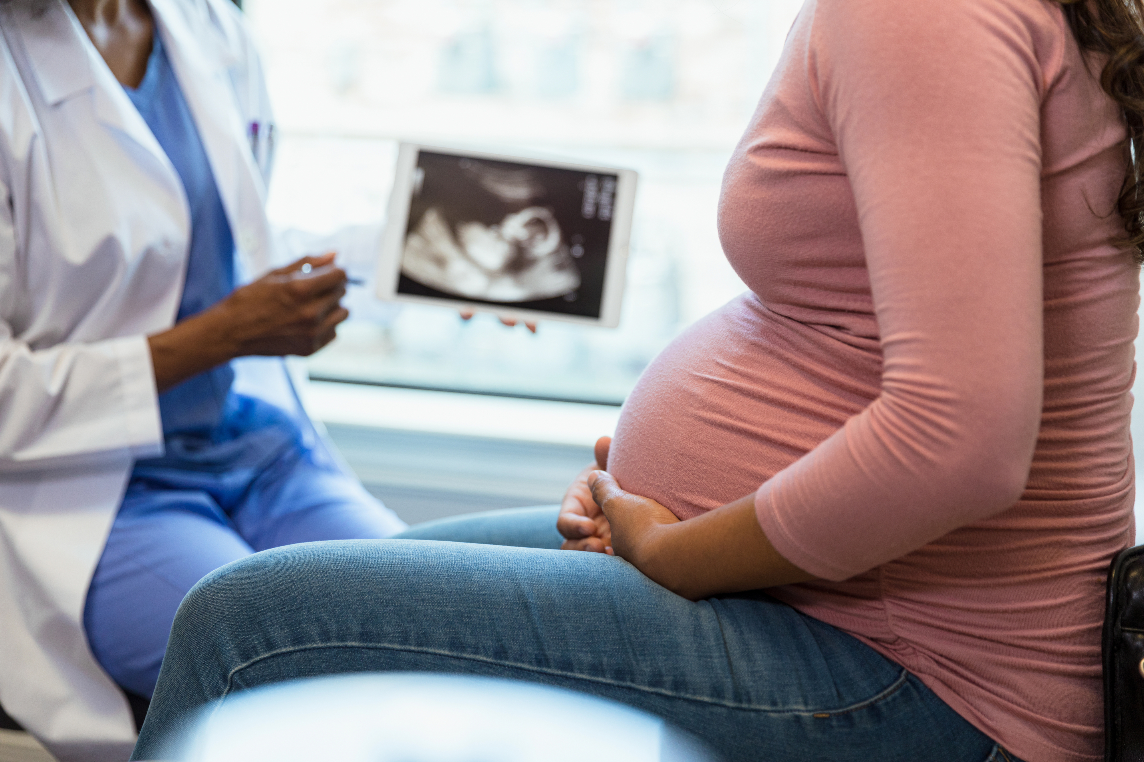 Pregnant person sitting with a doctor who is holding an ultrasound image
