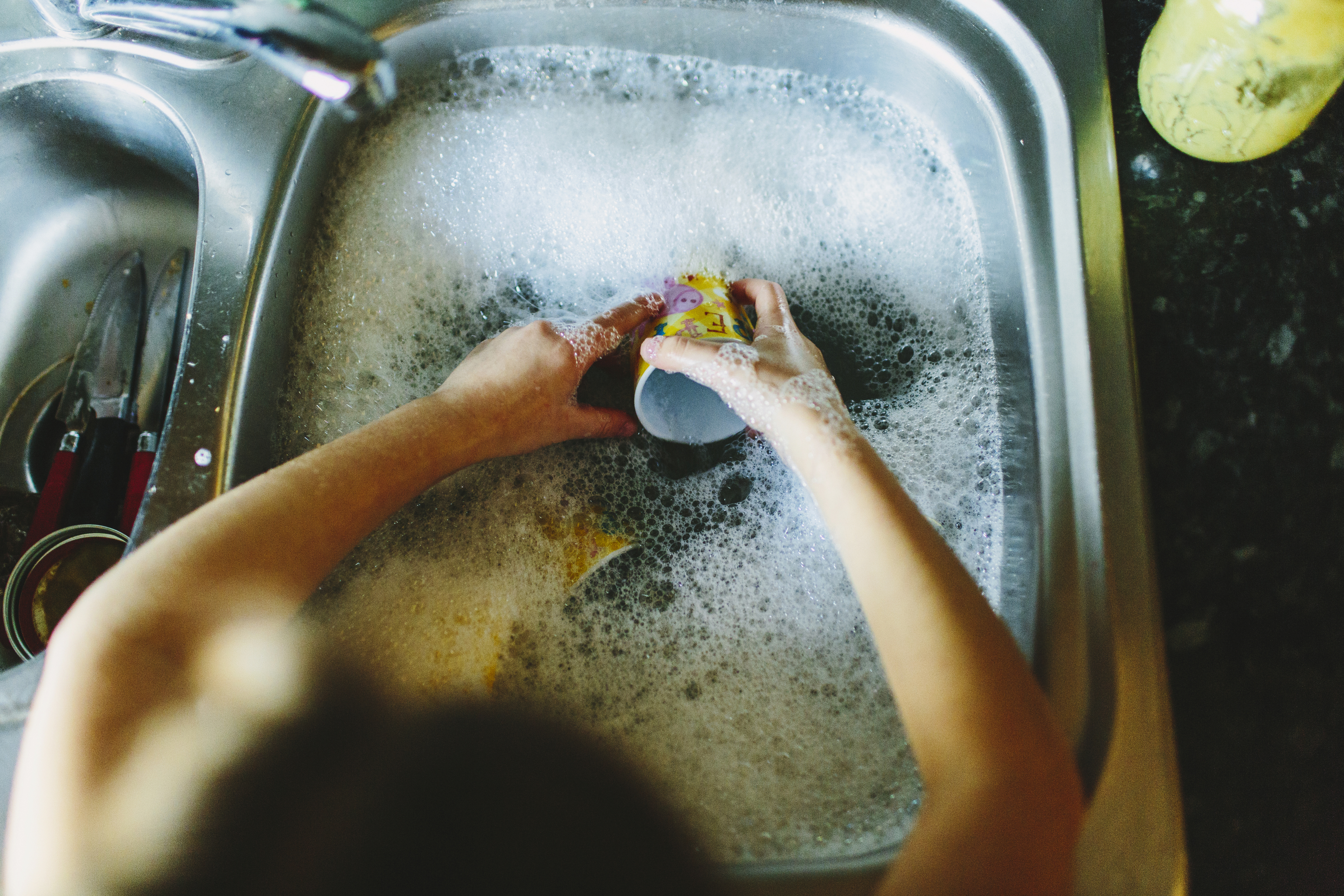 Person washing a cup in a kitchen sink filled with soapy water