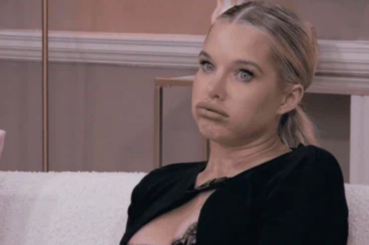 I don’t know who this is, but a woman with a neutral expression, sitting in a room setting, wearing a black top with lace details