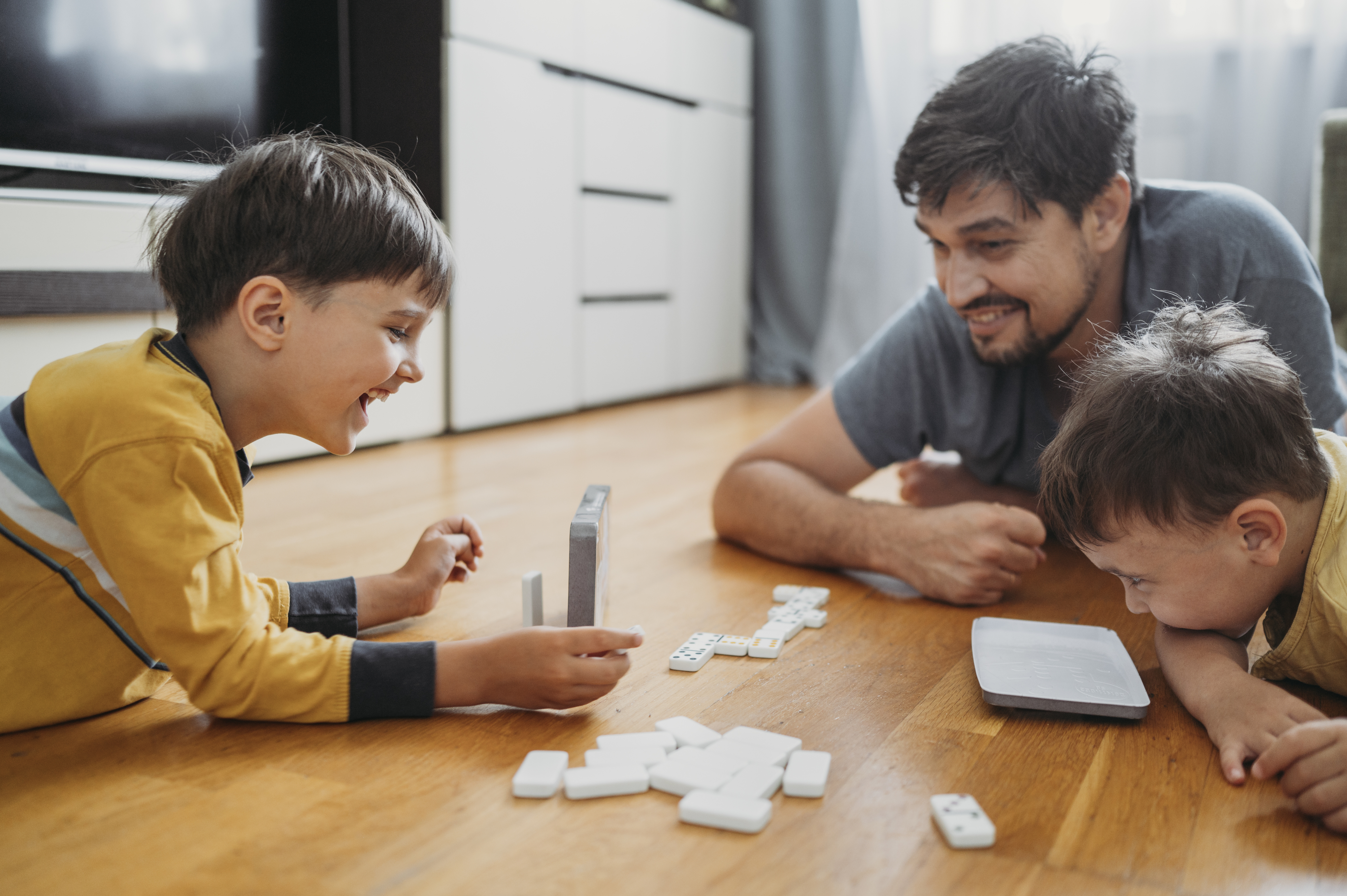 A man and two children play with dominoes on the floor, smiling and enjoying their time together