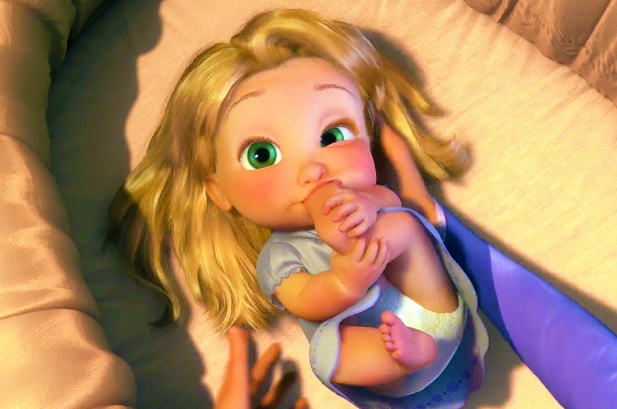 Baby Rapunzel from Tangled, with big eyes and blonde hair, lies in a crib sucking her toe