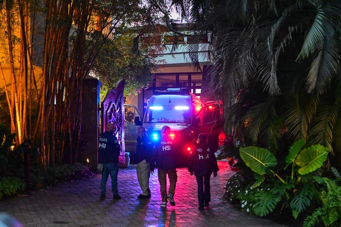 Police and Homeland Security officers walk toward a building at night, illuminated by red and blue lights