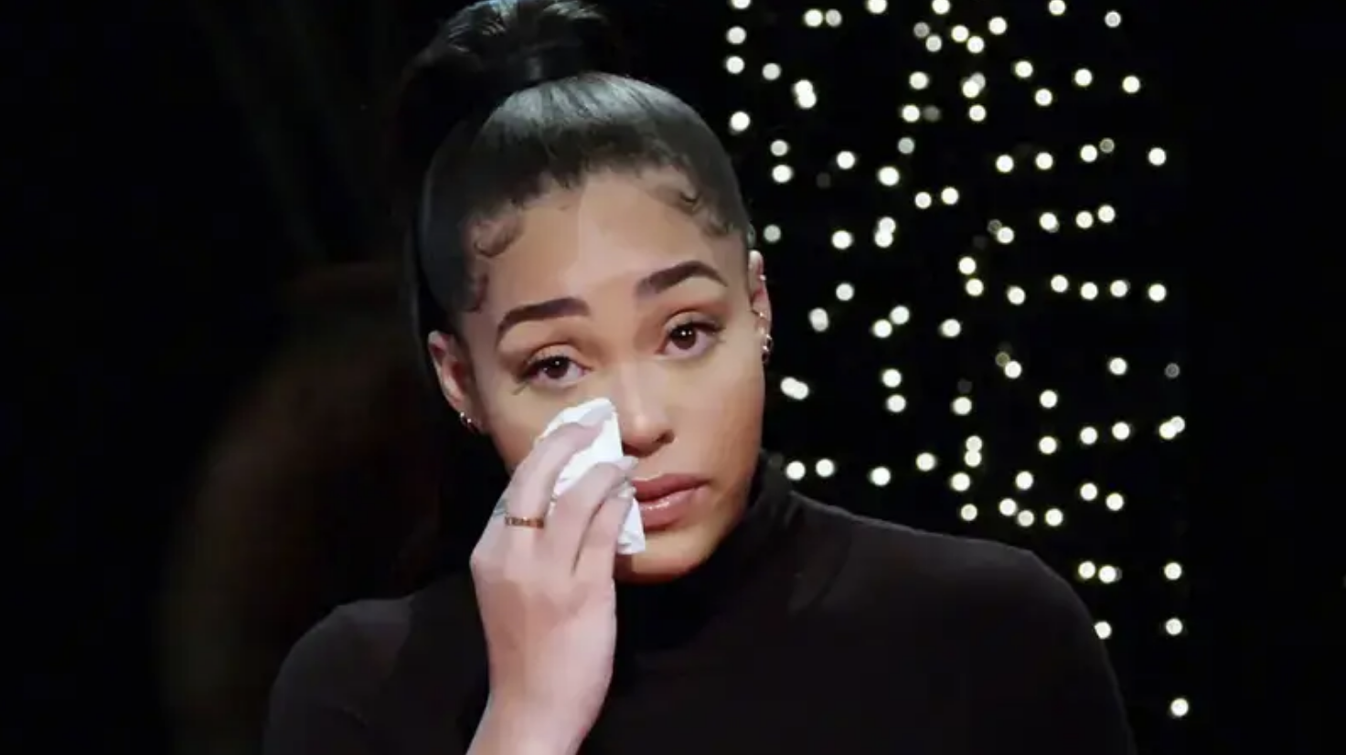 A person wipes their eye with a tissue, looking contemplative, against a dark backdrop with soft lights