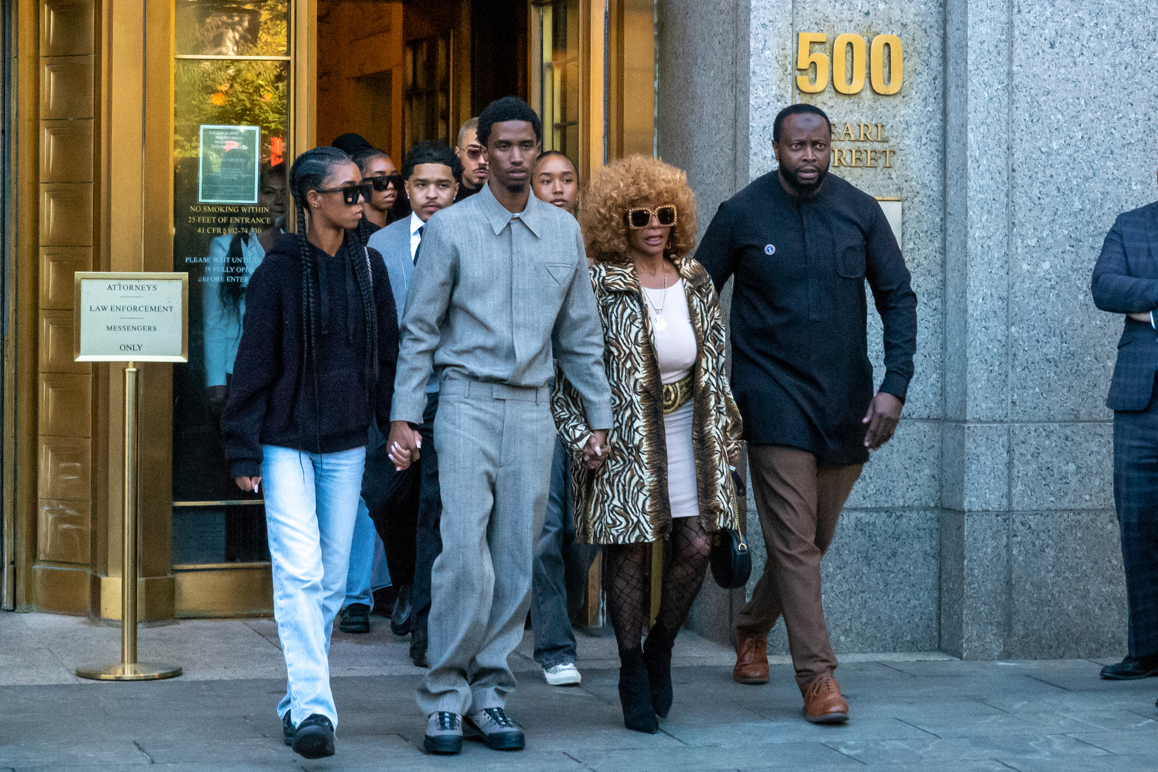 I don&#x27;t know who they are. A group of people walks outside a building; one person in zebra-print clothing, others in casual and formal wear