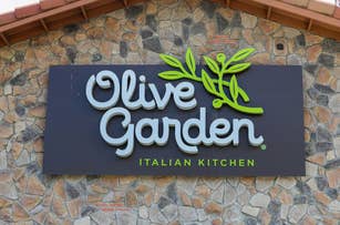 Sign with "Olive Garden Italian Kitchen" logo on a stone wall background