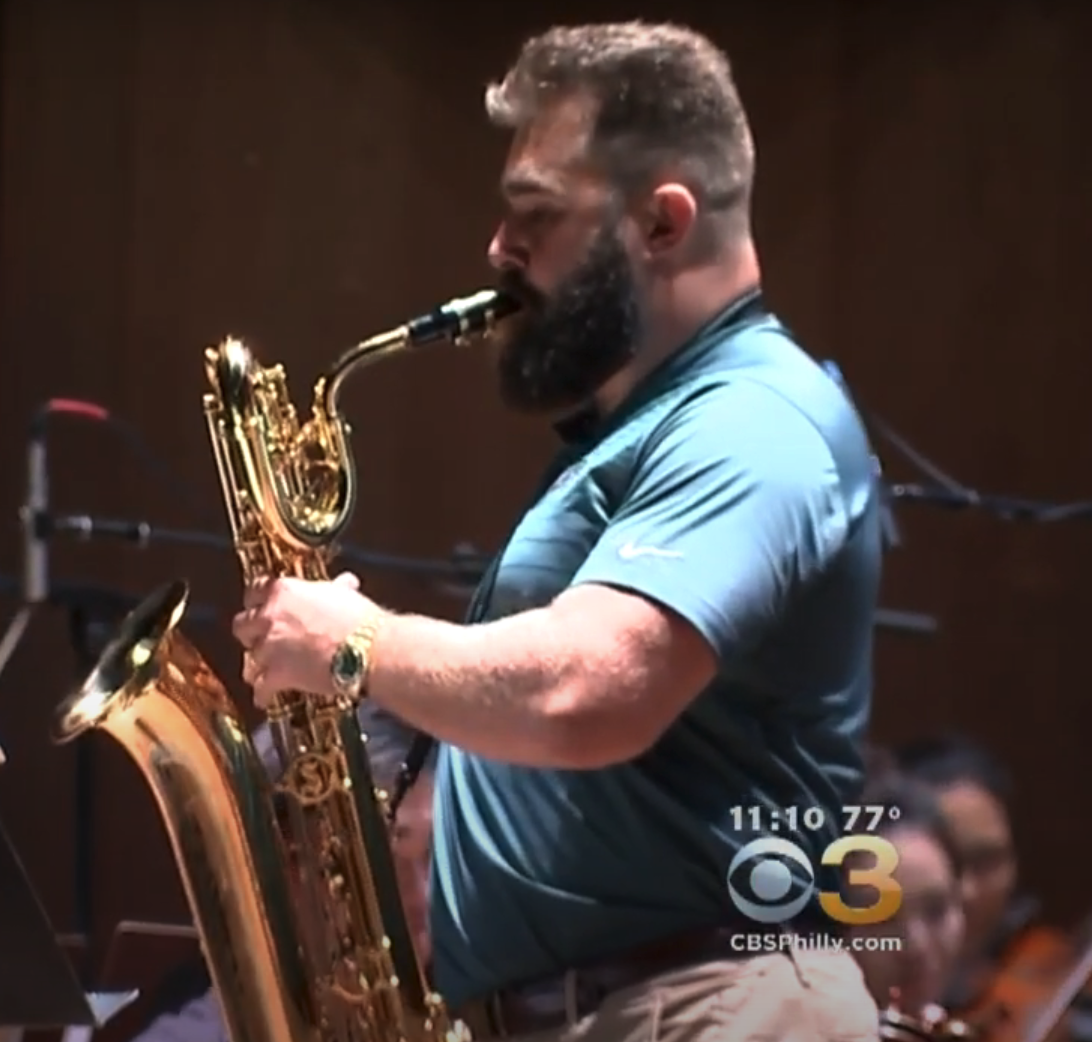 A musician plays the saxophone on stage during a live performance. CBS Philly logo is visible