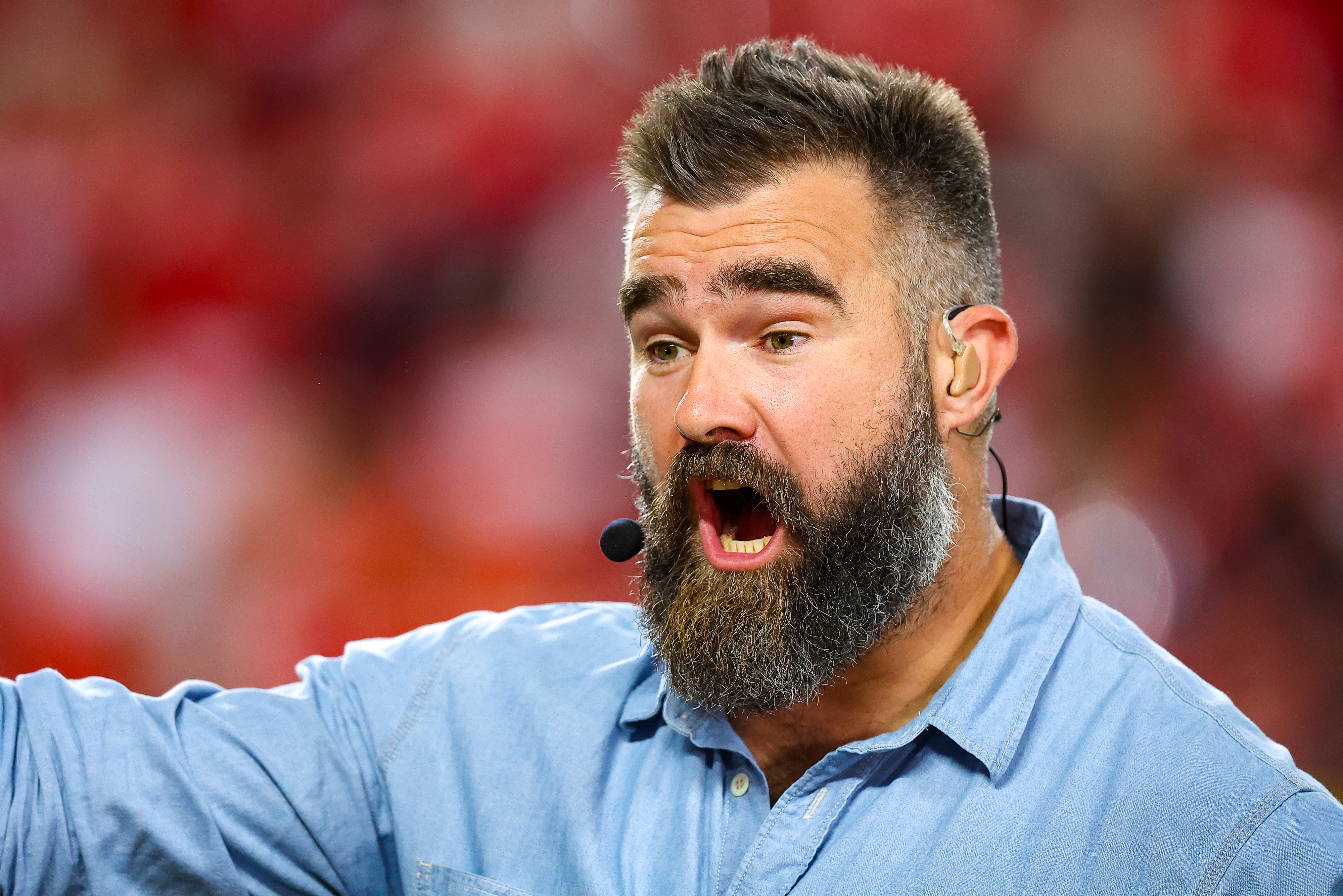 A man with a beard and wearing a denim shirt speaks passionately into a microphone during a public appearance