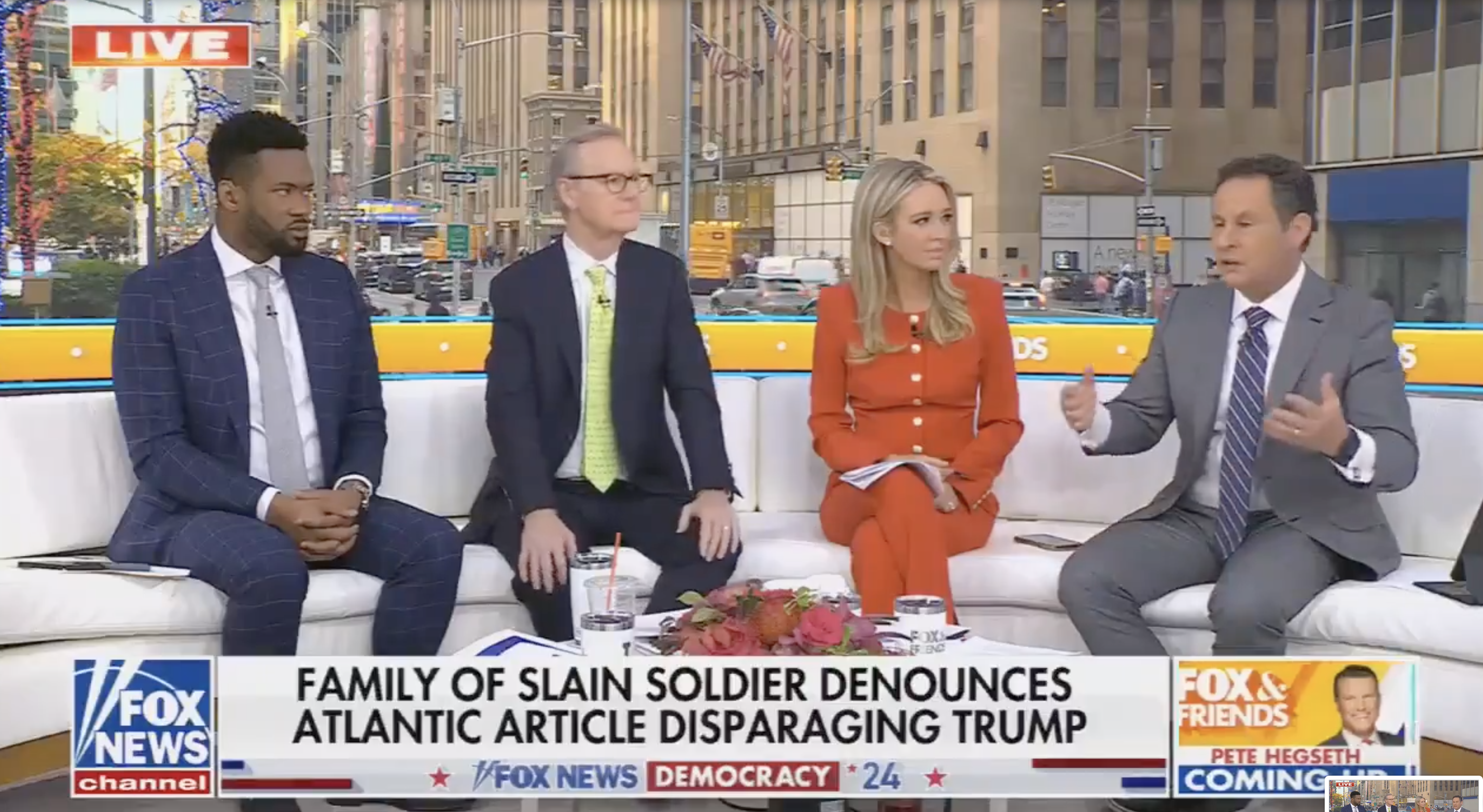 Four news anchors sit on a sofa discussing a news headline