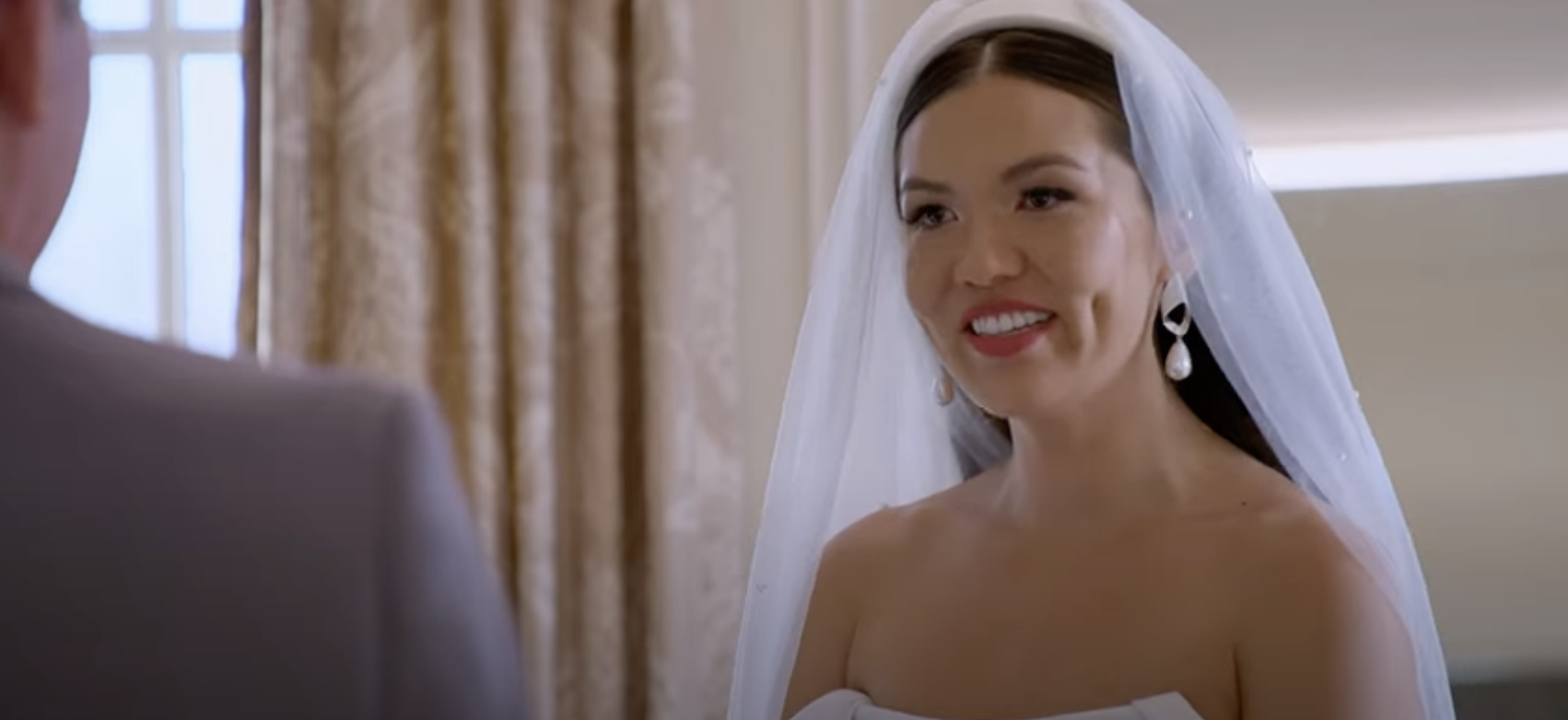 Taylor from Love Is Blind wearing a strapless gown and veil smiles during a wedding ceremony scene