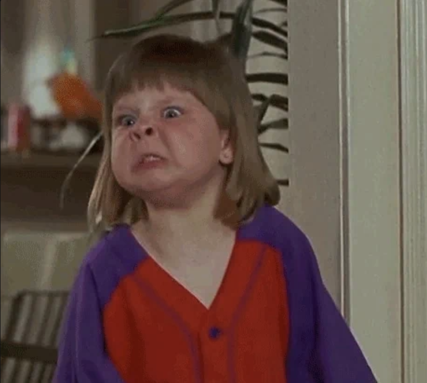 A young child making a funny, scrunched-up face indoors, wearing a two-toned shirt