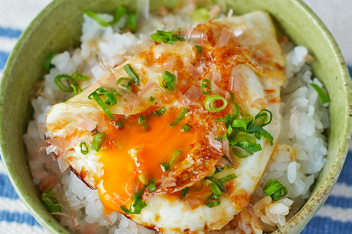 ご飯の上に半熟の目玉焼きがのった一杯の料理。刻んだネギと醤油がかかっています。