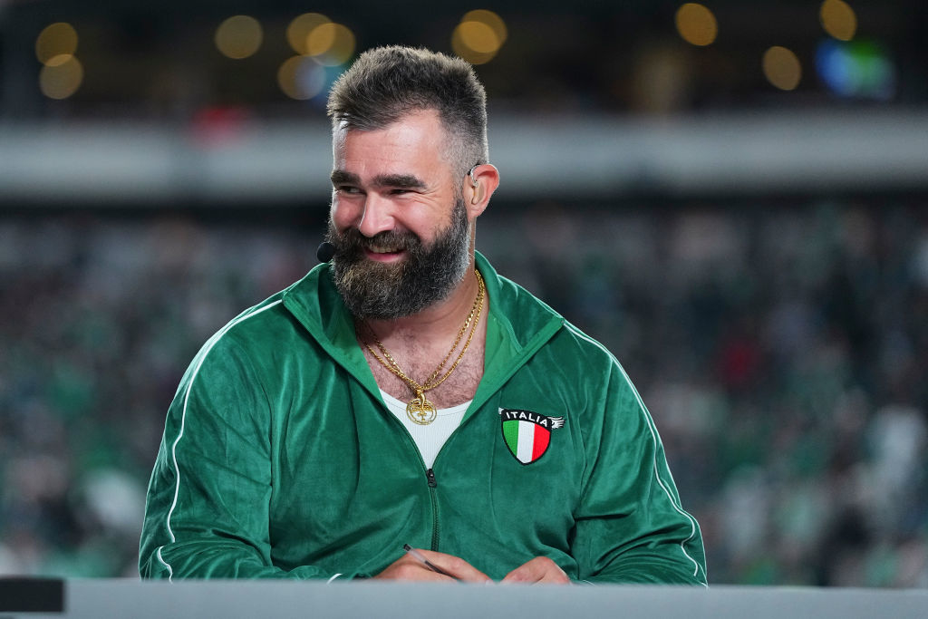 Close-up of Jason Kelce smiling on a football field, wearing a track jacket with a patch that reads "Italia"
