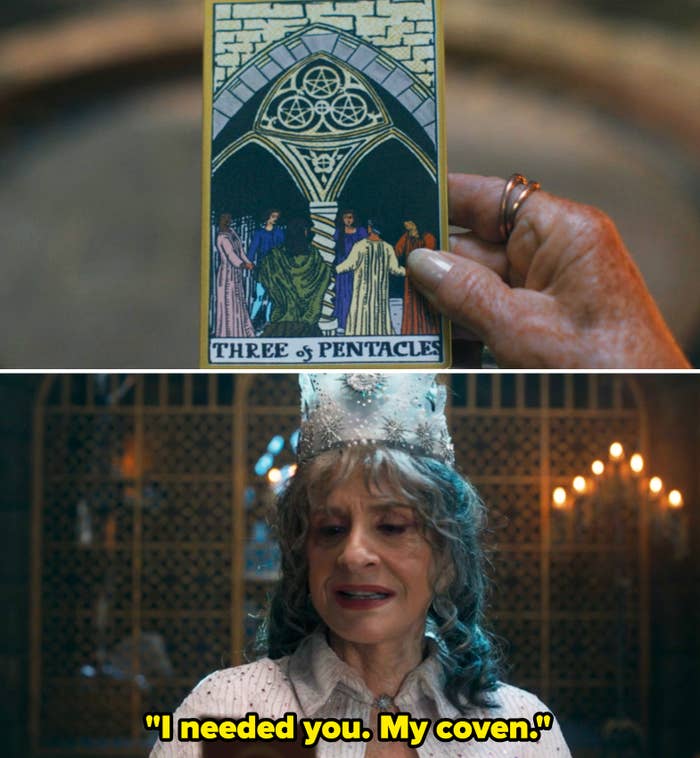 An older woman wearing a crown holds a tarot card,