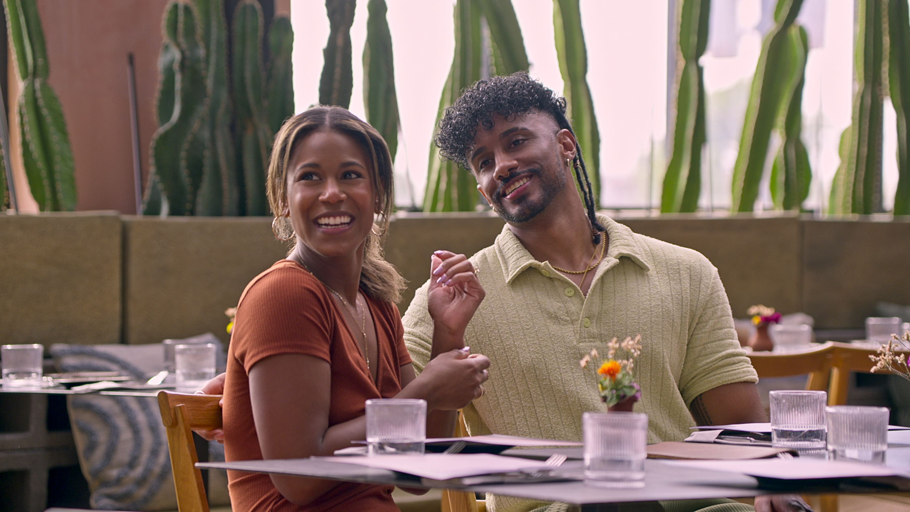 Two people smiling and sitting at a restaurant table with cacti in the background