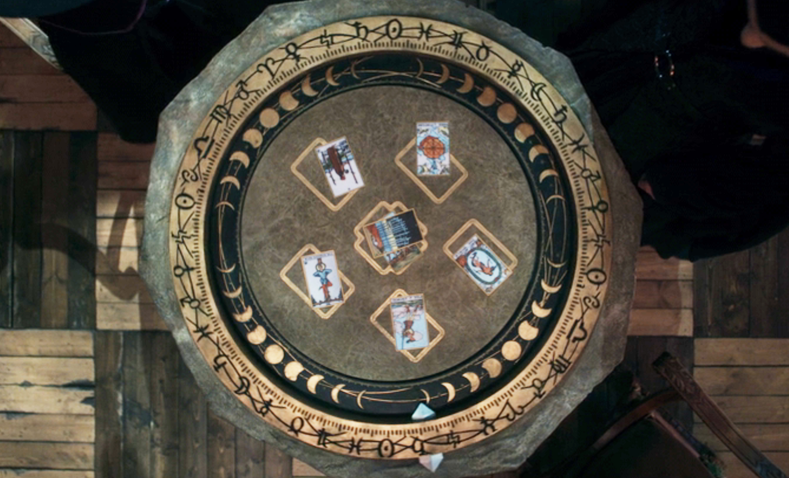 A round table with a zodiac wheel design holds six tarot cards, each depicting a unique figure or symbol, representing a tarot reading scene