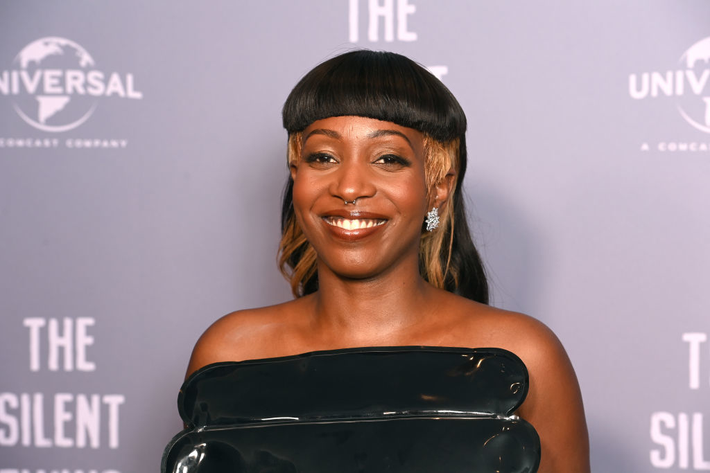 A person in stylish, strapless attire smiles on the red carpet at a Universal event backdrop