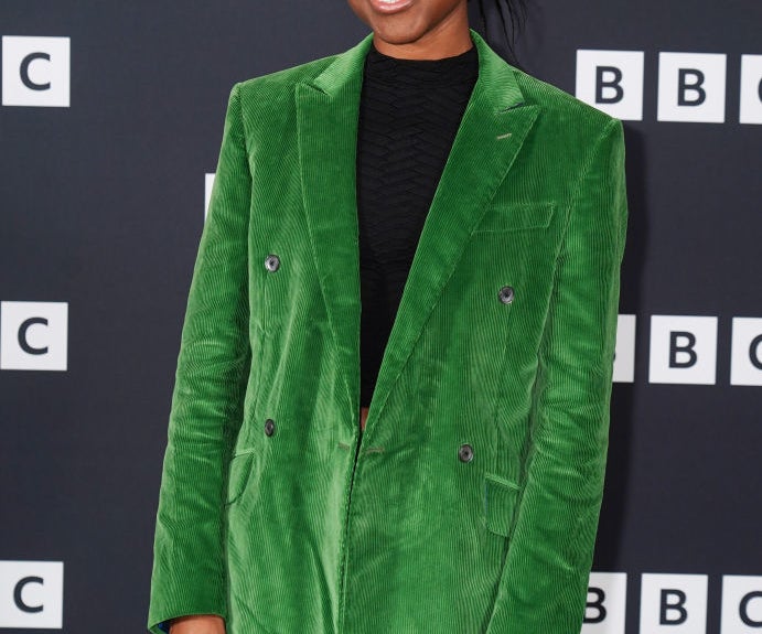 A person in a green corduroy suit poses at a BBC event backdrop, smiling