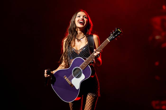 A musician performs on stage with a guitar, wearing a sequined outfit and fishnet tights