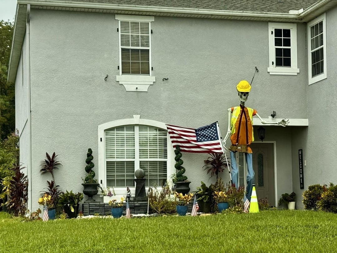 Skeleton dressed successful  operation  cogwheel  holds an American emblem  extracurricular  a grey  location   with achromatic  trim, surrounded by tiny  U.S. flags and plants