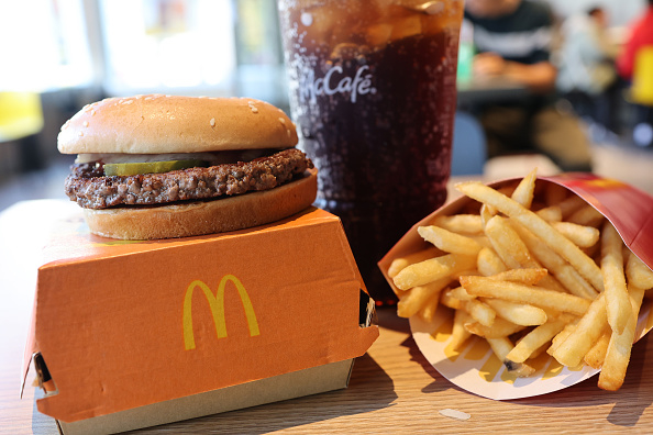 A McDonald&#x27;s burger on a box, fries in a carton, and a large drink in a McCafé cup on a table in a restaurant setting