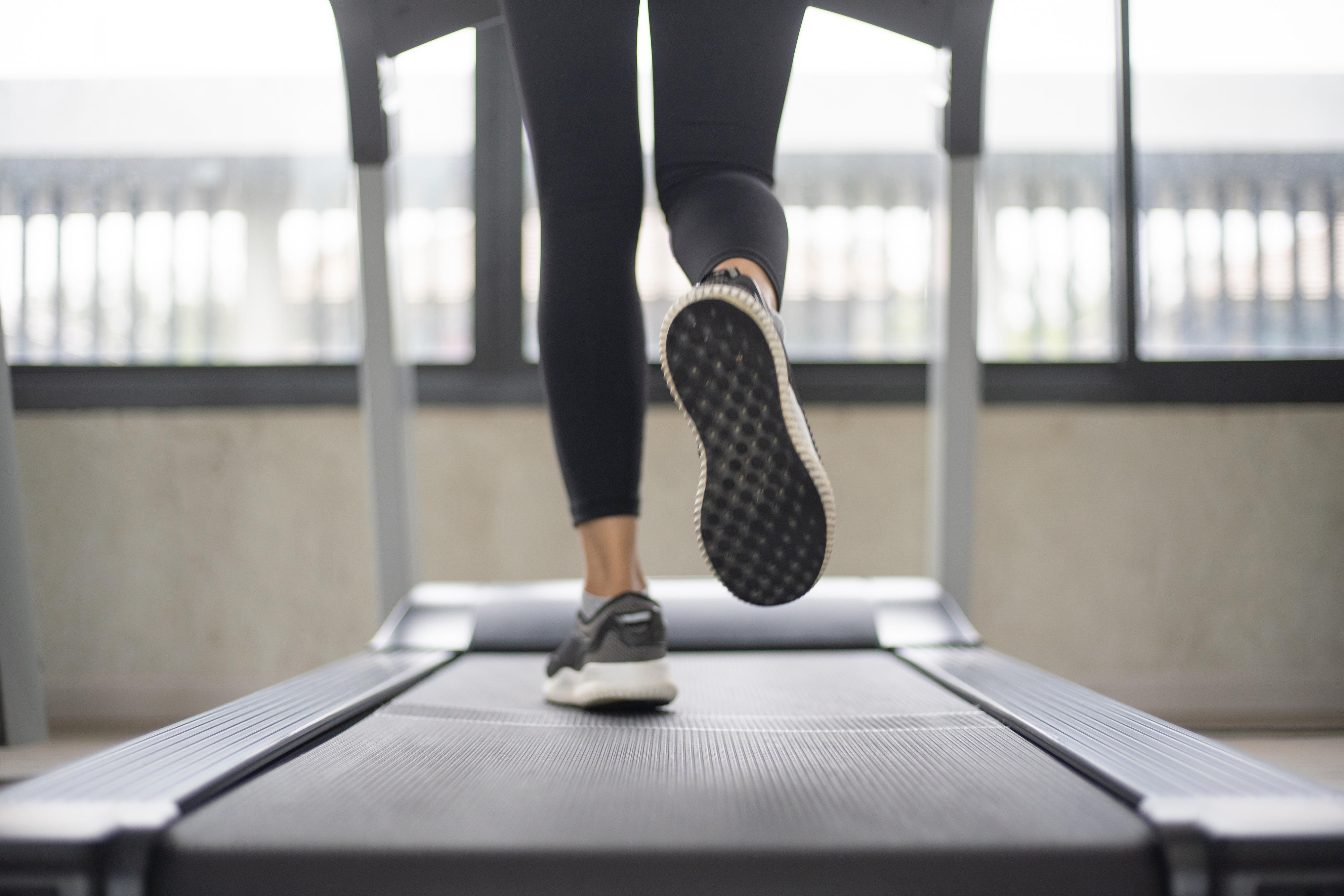 Person wearing sneakers running on a treadmill indoors