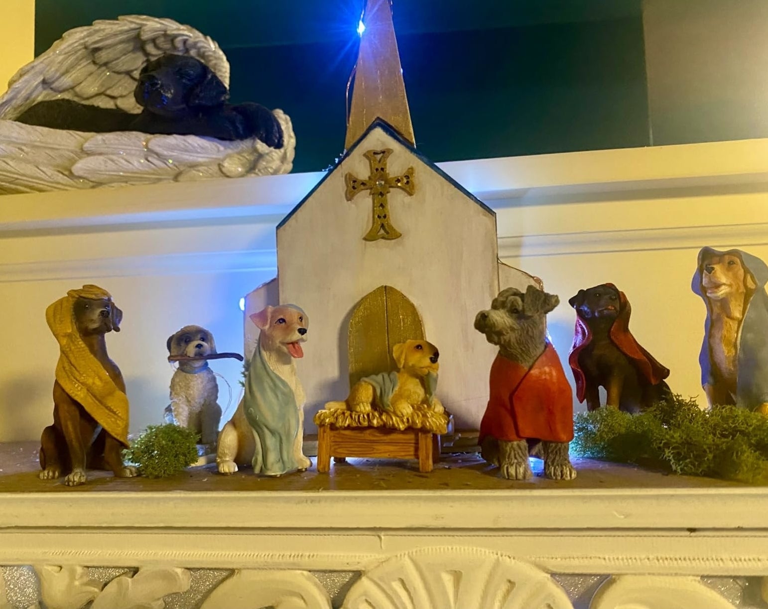 Nativity scene with dog figurines dressed as biblical characters arranged around a manger in front of a church backdrop