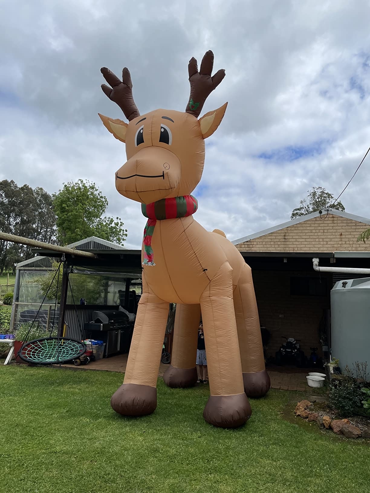 Giant inflatable reindeer with a scarf standing in a backyard near a house