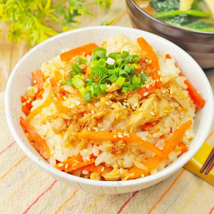 野菜と鶏肉の御飯。刻み葱とごまが上に載っている。奥に味噌汁。