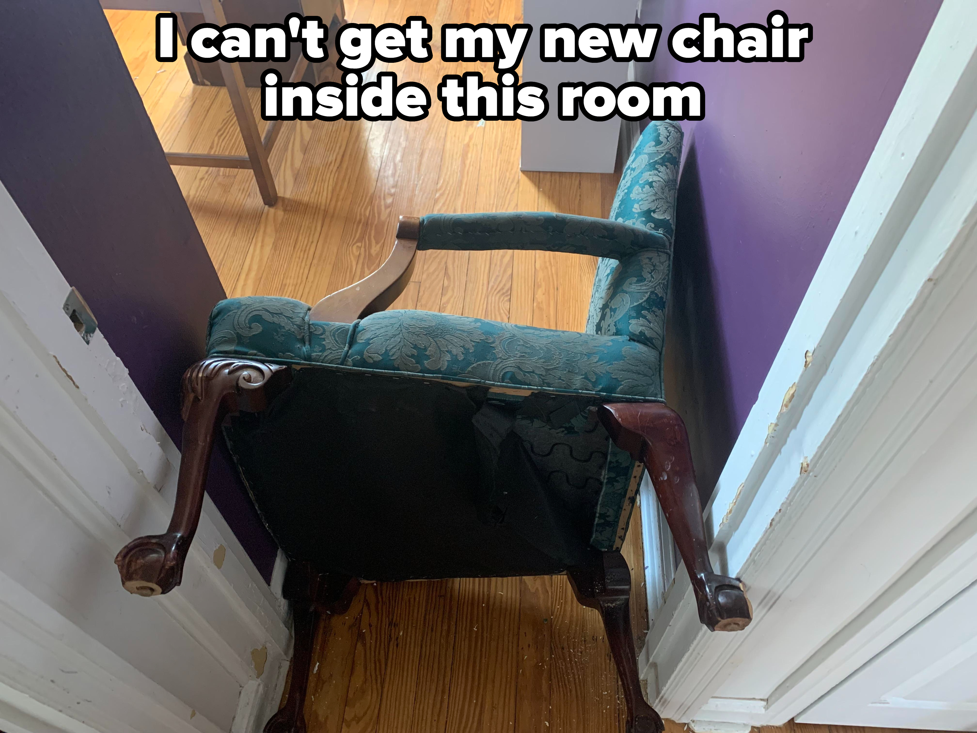 A chair is stuck diagonally in a narrow doorway between a purple wall and a white doorframe on a wooden floor