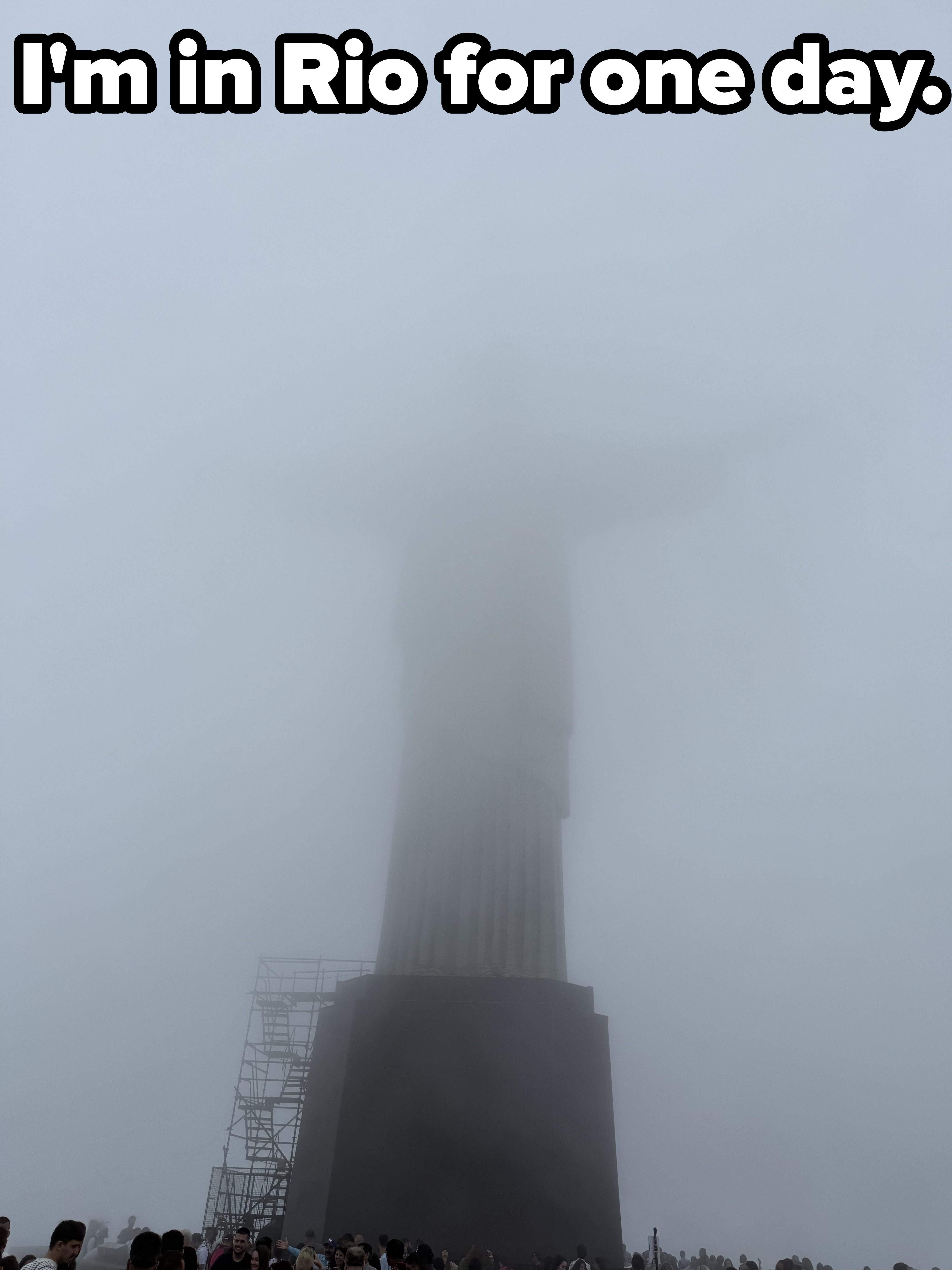 Foggy view of the Christ the Redeemer statue, partially obscured, with a crowd in the foreground