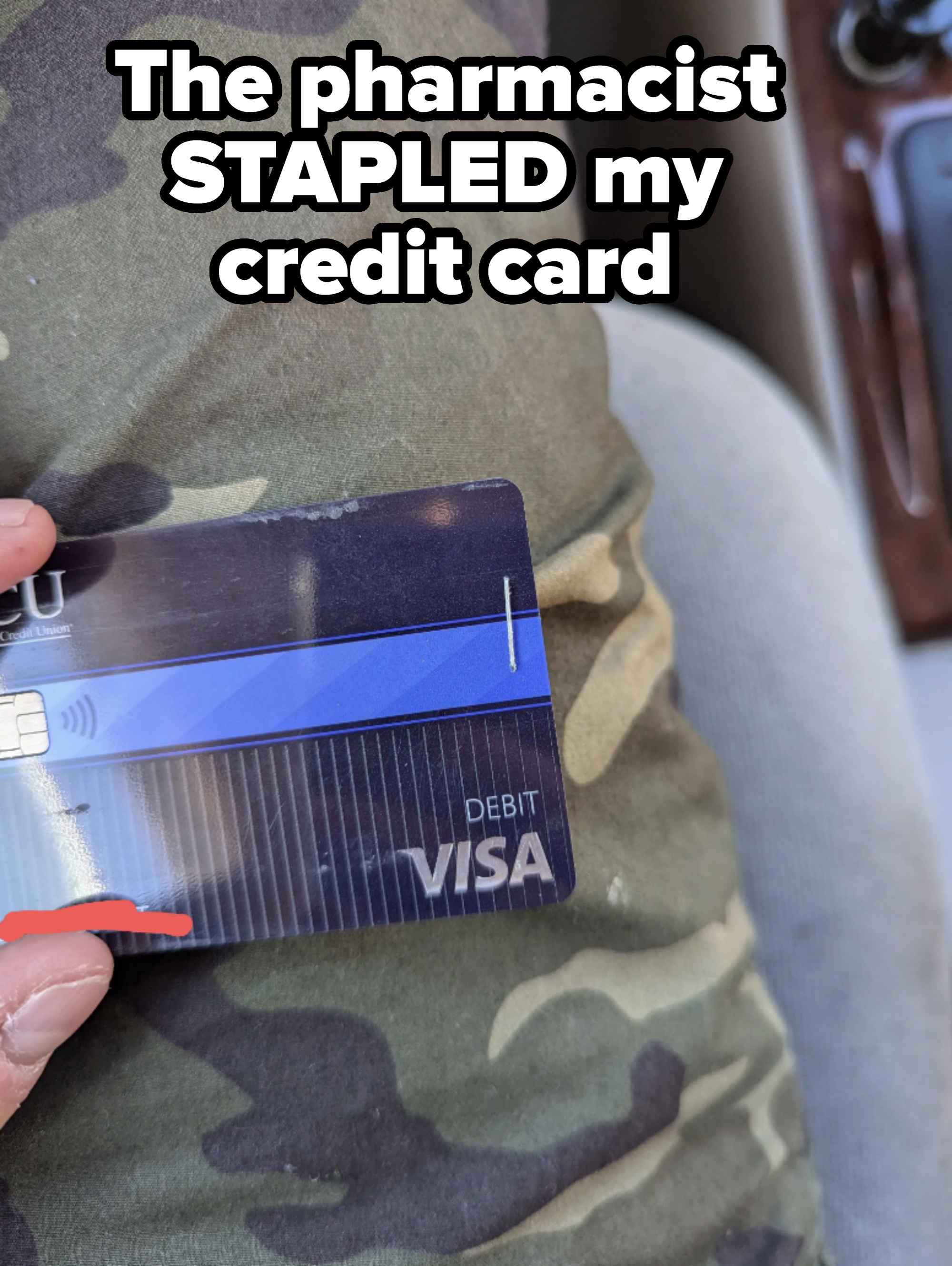 Person holding a Visa debit card with a camouflage-patterned background