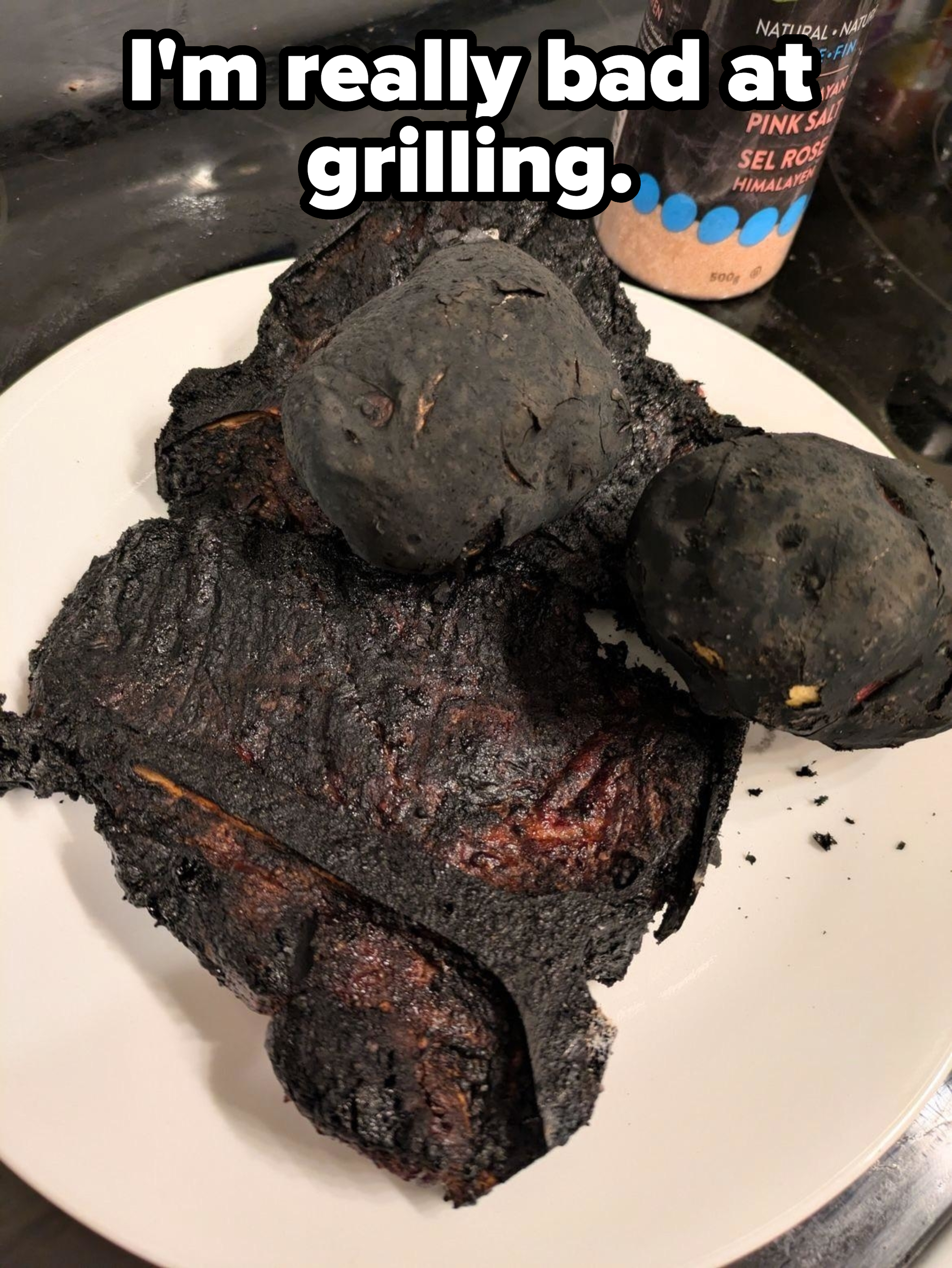 Charred food on a white plate, with a container of Himalayan pink salt in the background