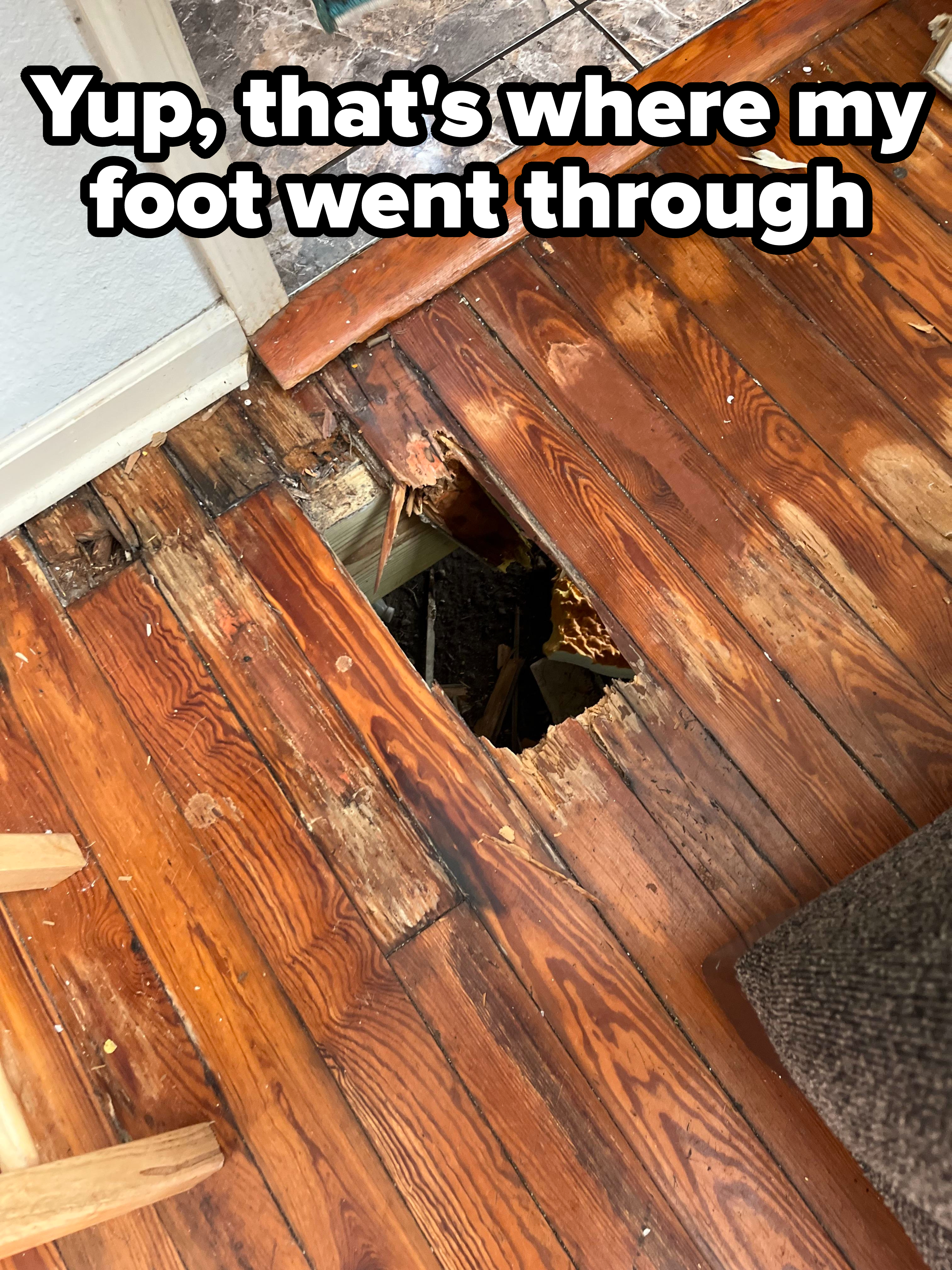 Wooden floor with a broken plank revealing a hole. Nearby floorboards appear worn and damaged
