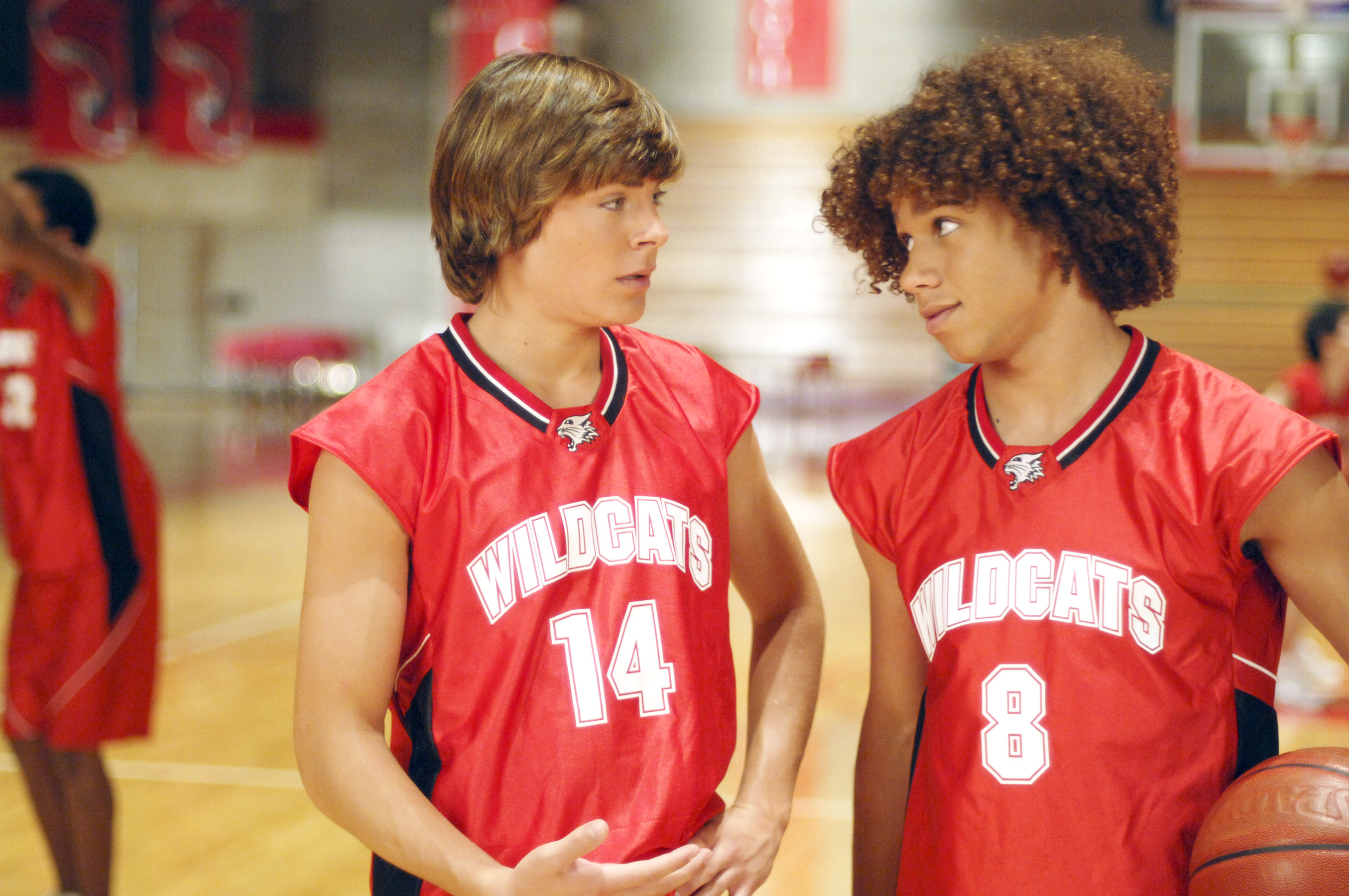 Two people in Wildcats basketball uniforms speaking on a gym court