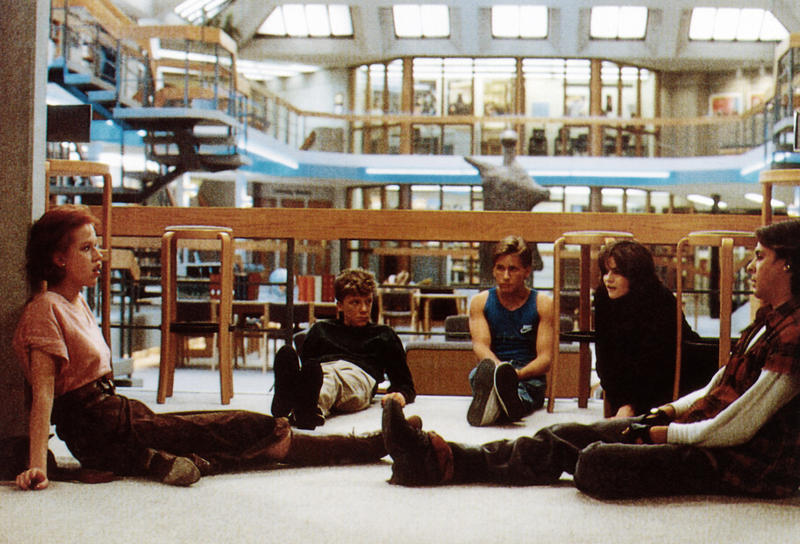 Five teenagers sit on the floor of a library in a discussion, from a scene in "The Breakfast Club."