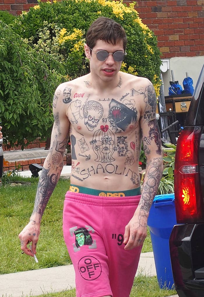 Pete Davidson walks shirtless in shorts and sunglasses near a truck