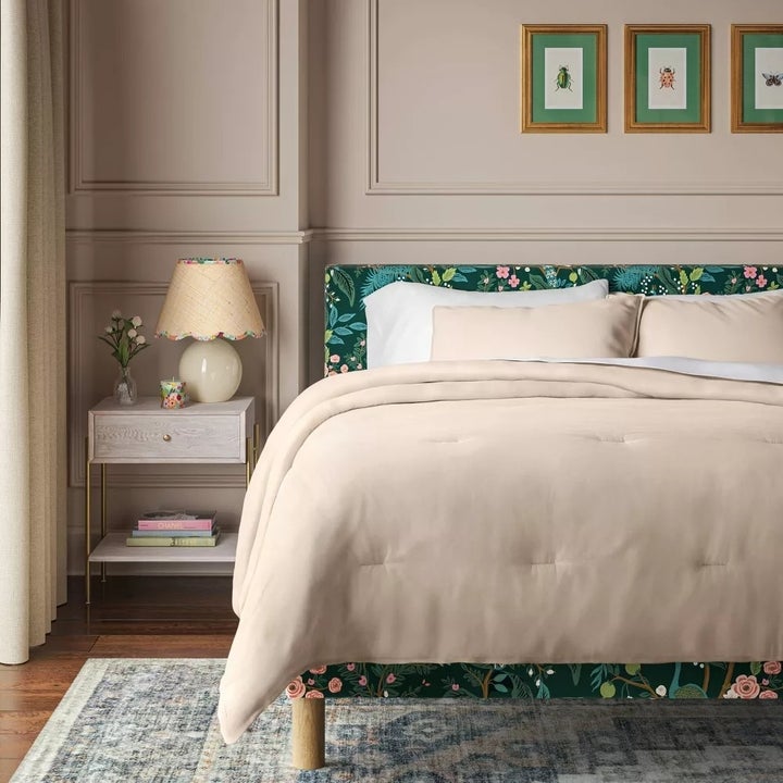 Modern bedroom with floral-patterned bed, soft beige bedding, and a lamp on bedside table. Framed botanical art is mounted on the wall above